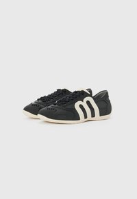 Black athletic shoes with leather and textile upper, rubber sole, distinctive cream-colored design accents, and perforated details.