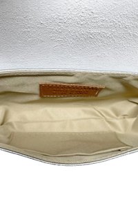 Interno di borsa bianco testurizzato con fodera beige; presenta un'etichetta in pelle marrone chiaro e una forma elegante con dettagli di cucitura.