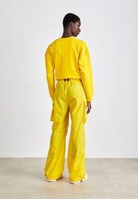 Felpa gialla con spalle raglan e pantaloni cargo gialli abbinati, dotati di tasche laterali e cintura elastica, visti da dietro.