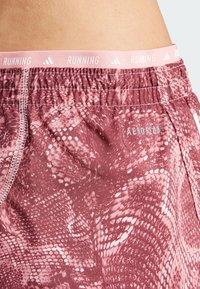 Bordeaux hardloopshorts met een slangenhuidpatroon, elastische tailleband met "RUNNING" en "AEROREADY" branding, gladde textuur.