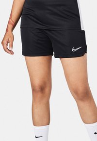Pantaloni sportivi neri realizzati in un tessuto liscio, con un logo Nike bianco in basso a sinistra. Il design include una cintura elastica.