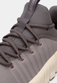 Γκρι αθλητικό παπούτσι με υφασμάτινο άνω μέρος με υφή, επίπεδους κορδόνια και αντίκτυπη ανοιχτόχρωμη σόλα. Περιλαμβάνει λεπτές ανάγλυφες λεπτομέρειες στο πλάι.