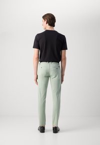 Svijetlozelene krojene hlače slim fit kroja, s mid-rise strukom, stražnjim džepovima i glatkom teksturom tkanine, u kombinaciji s crnom majicom.
