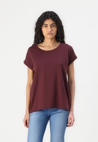 Tricou scurt cu mânecă din bumbac crocant, culoare burgundy, cu o croială lejeră, decolteu rotund, hem ușor căzut, asortat cu blugi de culoare albastru deschis.
