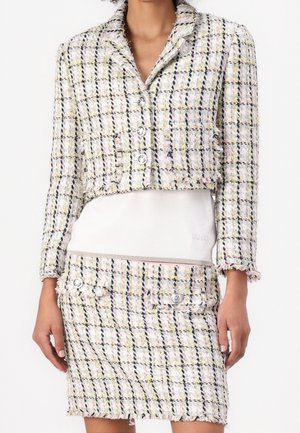 Donna che indossa un blazer corto a quadri pastello con bottoni d'argento e gonna a vita alta abbinata sopra una maglietta bianca.