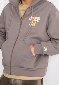 Gray zip-up hoodie made of cotton blend, featuring a colorful graphic on the chest, kangaroo pocket, and Nike logo on the sleeve.
