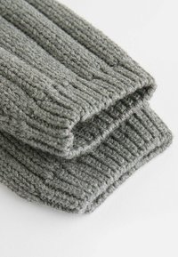 Polsini grigi lavorati a maglia con una trama a coste, che mostrano un filato spesso e morbido. I bordi sono cuciti con cura, evidenziando il calore del tessuto.