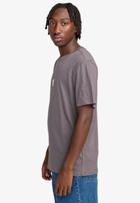 Camiseta de algodón gris con cuello redondo, mangas cortas y un diseño gráfico en el frontal. Se lleva con jeans de mezclilla azules.