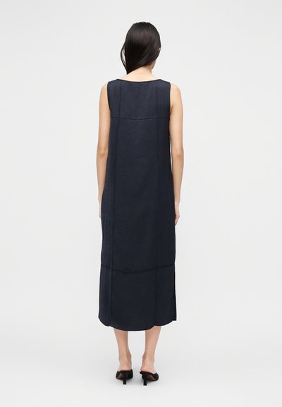 Varrukateta, pikk tumesinine kleit sirge silueti ja peene tekstuuriga. Omab ümarat kaelust ja külje lõhikumisi, kantud mustade kontsakingadega.