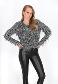 Pulover negru și alb cu franjuri, gât rotund, mâneci lungi și suprafață texturată, asortat cu colanți negri și cercei argintii.