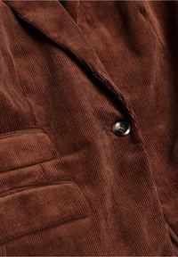 Blazer in corduroy marrone con texture a righe verticali, rever, chiusura con un bottone e tasca laterale. Finitura del tessuto liscia.