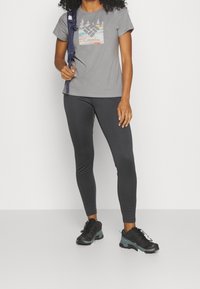 Grå Columbia-t-shirt med en berggrafik, kombinerad med svarta leggings och robusta svarta vandringsskor med tealaccenter.
