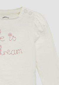 Weißes Langarm-Babyshirt mit Druckknöpfen an der Schulter und rosa gesticktem Text sowie Blütendetail auf der Vorderseite.