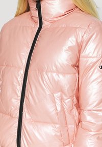 Rosa, glänsande puffjacka med hög krage, svart dragkedja och sidofickor. Har quiltade sektioner för isolering.