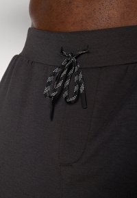 Donkergrijze loungebroek met een elastische tailleband en een zwart-grijze trekkoord. Gladde textuur met een subtiele glans en zijzak.