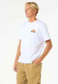 White cotton t-shirt featuring a colorful Rip Curl logo on the left chest, paired with beige corduroy pants. Simple design and relaxed fit.