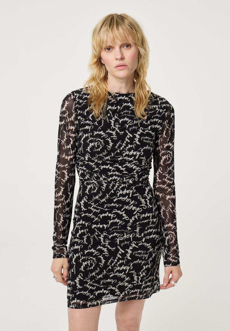 Zwarte jurk met lange sheer mouwen, voorzien van een gerimpeld ontwerp en een wit handgeschreven patroon over de hele jurk. Aansluitende silhouet met een ronde halslijn.