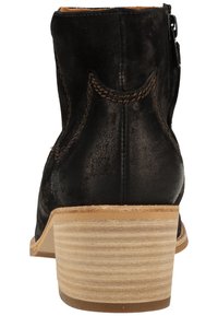 Botín negro de ante con tacón de madera apilado y costuras marrones visibles, visto desde atrás.