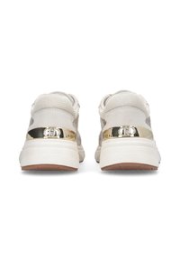 Par de zapatillas beige con suelas blancas gruesas, tejido de malla, detalles de serraje y acentos dorados reflectantes en el talón vistos desde la parte trasera.
