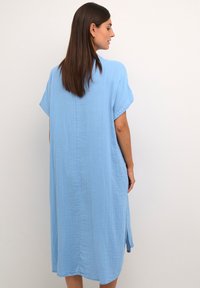Šviesiai mėlynas, iki kelių ilgio suknelė iš tekstūruotos medžiagos, su trumpomis rankovėmis ir šoninėmis plyšiais, turinti paprastą, laisvą siluetą.
