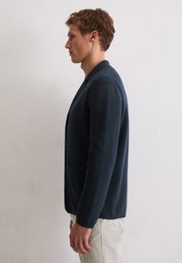Marineblauer Cardigan aus strukturiertem Strickstoff. Verfügt über einen Ein-Knopf-Verschluss mit drei Knöpfen und zwei vorderen Taschen.