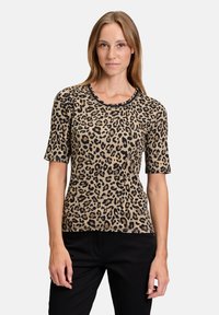 Haut à manches courtes en imprimé léopard dans des tons de beige et noir, avec un col rond et une coupe ajustée, associé à un pantalon noir.