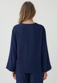 Navyblaues Langarmoberteil aus leichtem Stoff mit geradem Schnitt und weiten Ärmeln, rundem Ausschnitt und minimaler Detailgestaltung.