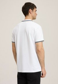 Biała koszulka polo z czarnymi wykończeniami na kołnierzyku i rękawach. Wykonana z bawełny, luźny krój, krótkie rękawy i prosty design.