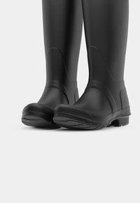 Bottes en caoutchouc noir avec une finition lisse, des bouts arrondis et des semelles texturées pour une meilleure adhérence, conçues pour un usage imperméable.