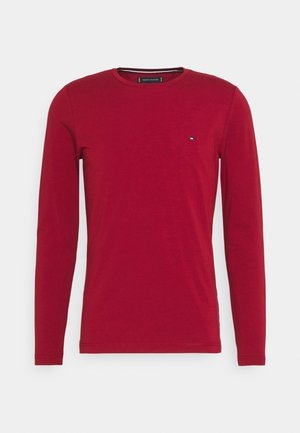 Męska czerwona koszulka z długim rękawem i okrągłym dekoltem z małym logo Tommy Hilfiger na lewej piersi na białym tle.