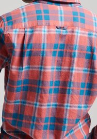 Flannel shirt featuring a large plaid pattern in coral, blue, and purple. Soft texture with a button-down collar and a loop at the back.
