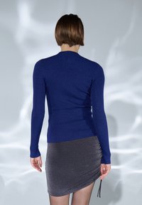 Dunkelblaues geripptes Sweatshirt mit langen Ärmeln, kombiniert mit einem silbernen metallic gerafften Rock mit einem Kordelzugdetail an der Seite.