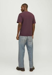 Camiseta de algodón morado oscuro combinada con jeans de mezclilla azul claro; la camiseta tiene mangas cortas y un cuello redondo estándar.