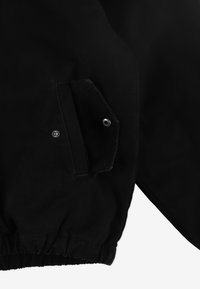 Czarna kurtka z teksturowanej tkaniny, elastycznymi mankietami i kieszenią zapinaną na nap na lewej stronie. Prosty, funkcjonalny design.