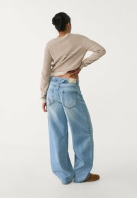 Beige-värinen raidallinen neule yhdistettynä väljiin, vaaleansinisiin farkkuihin. Farkuissa on korkea vyötärö, takataskut ja haalistunut pinta.