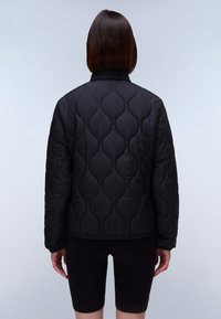 Black quilted jacket featuring curved pattern stitching, high collar, and elastic hem. The fabric is smooth and slightly shiny.