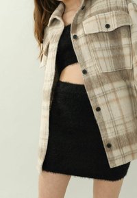 Beige and white plaid flannel shirt jacket with black buttons, layered over a black fuzzy crop top and mini skirt. Textured details visible.
