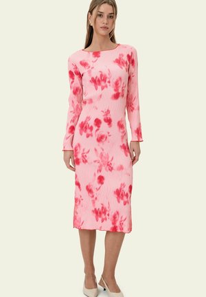 Frau trägt ein rosa Midikleid mit langen Ärmeln und roten Blumenmustern, kombiniert mit beigen Slingback-Schuhen mit niedrigem Absatz.