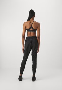 Czarny sportowy biustonosz z krzyżującym się z tyłu wzorem i wycięciem. Czarne spodnie dresowe z białymi bocznymi paskami i elastycznym pasem. Oba wykonane z gładkiego materiału.