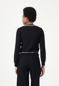 Maglione nero con maniche lunghe, bordi bianchi lungo il colletto e l'orlo. Il tessuto sembra liscio; design aderente con una leggera elasticità.