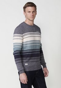 Heren gebreide trui met horizontale strepen in marineblauw, crème en teal. Bevat een ronde hals en ribbelmanchetten voor textuur.