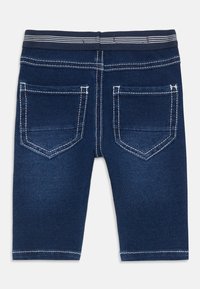 Jeansshorts i mörkblått med en slät yta, har två bakfickor, vit sömnad och ett randigt elastiskt midjeband.