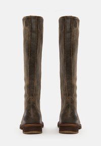 Bottes hautes en cuir marron vieilli avec coutures visibles et talons empilés en bois bas, vues de dos sur un fond blanc.