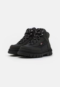 Czarne sneakersy w stylu high-top z teksturowanym wykończeniem, okrągłym noskiem, grubą gumową podeszwą oraz czarno-białymi sznurowadłami w wzory z akcentami logo.