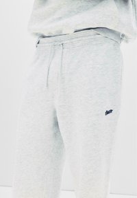 Lichte grijze sweatpants van zacht materiaal. Voorzien van een elastische tailleband en een klein donkerblauw logo op de linker bovenbeen. Minimalistisch ontwerp.