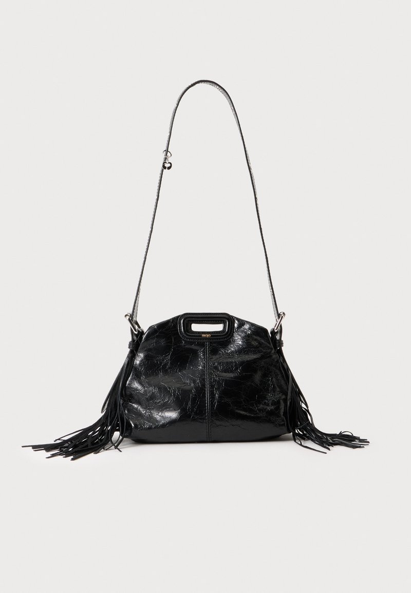 Sac à main en cuir noir brillant avec une longue fine bandoulière et des pompons à franges des deux côtés sur un fond clair.