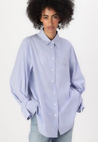 Blau-weiße gestreifte, oversized Hemdbluse mit Kragen, langen Ärmeln und einer Brusttasche, aus einem weichen Stoff gefertigt.