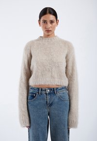 Beige, cropped sweater made of fluffy material, featuring long sleeves and a round neckline. Paired with light blue, high-waisted jeans.