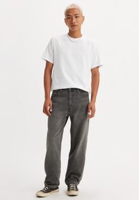 White cotton t-shirt, straight-cut dark gray jeans, and black canvas sneakers with white soles. Minimalist design and relaxed fit.