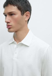Polo shirt bianco in cotone, con colletto classico, tre bottoni e maniche corte con una finitura leggermente testurizzata.